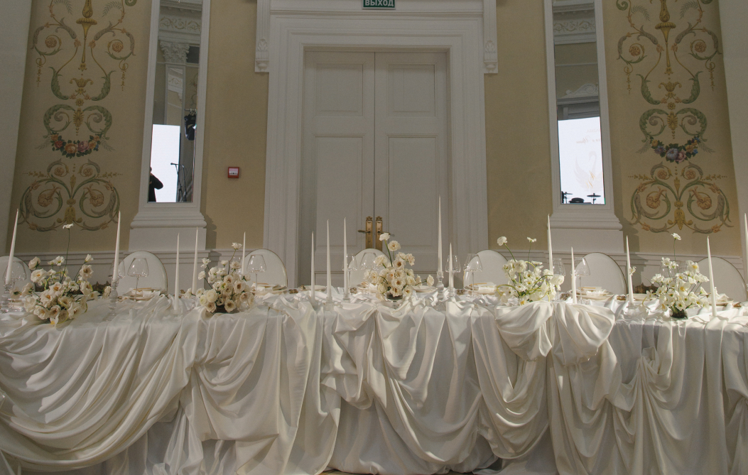 Стол декорированный для проведения свадьбы в белых тканях с драпировкой ткани